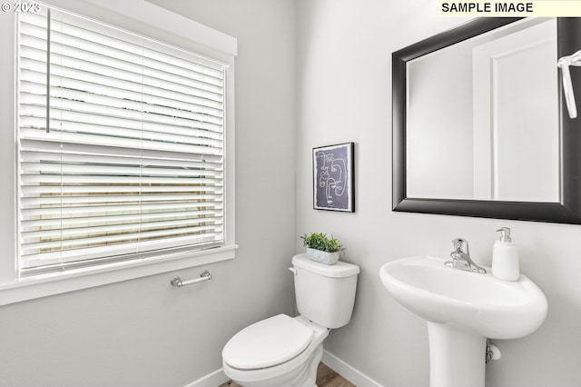 half bath with baseboards, toilet, and a sink