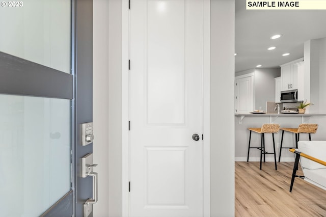 kitchen with stainless steel microwave, a kitchen bar, light wood finished floors, recessed lighting, and white cabinetry