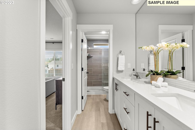 bathroom with a shower stall, toilet, double vanity, and wood finished floors