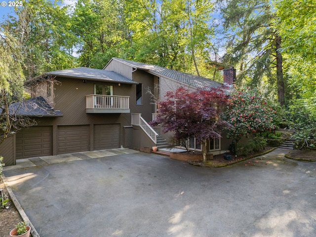 view of front facade featuring an attached garage, stairway, a chimney, a balcony, and driveway