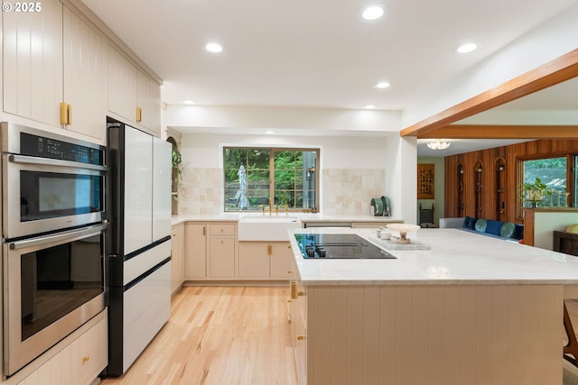 kitchen featuring freestanding refrigerator, double oven, black electric cooktop, tasteful backsplash, and a sink
