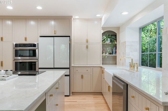 kitchen featuring light stone countertops, appliances with stainless steel finishes, a sink, and light wood-style flooring