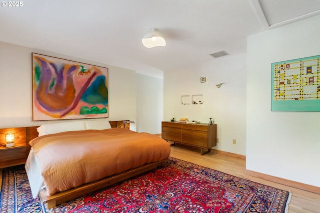 bedroom featuring visible vents, attic access, baseboards, and wood finished floors
