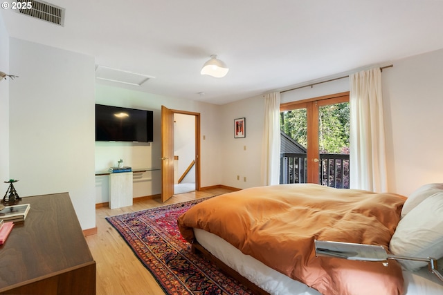 bedroom with access to exterior, attic access, baseboards, light wood-type flooring, and visible vents