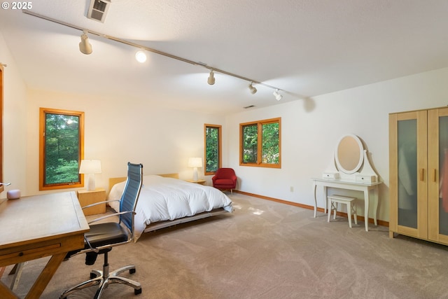 carpeted bedroom featuring track lighting, baseboards, and visible vents