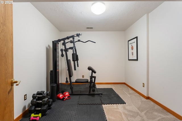 workout area with visible vents, carpet flooring, a textured ceiling, and baseboards
