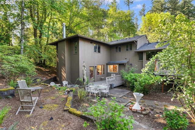 back of property with roof with shingles, a patio area, and a wooden deck