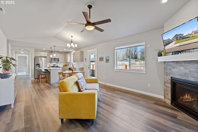 902 SE 3rd St, Prineville, OR 97754 - living room featuring a fireplace, vaulted ceiling, baseboards, wood finished floors, and ceiling fan with notable chandelier