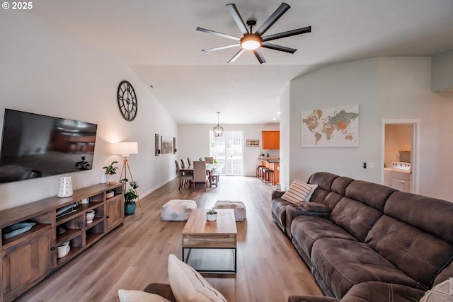 living room featuring baseboards, a ceiling fan, washing machine and clothes dryer, vaulted ceiling, and light wood-style floors