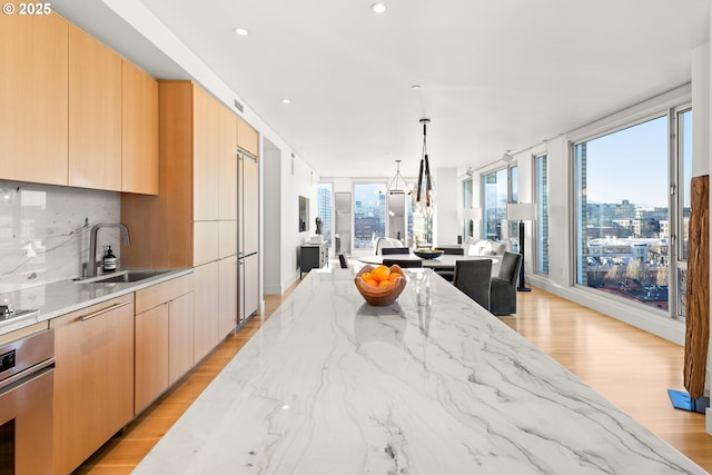 kitchen featuring sink, hanging light fixtures, light stone countertops, stainless steel oven, and light brown cabinets