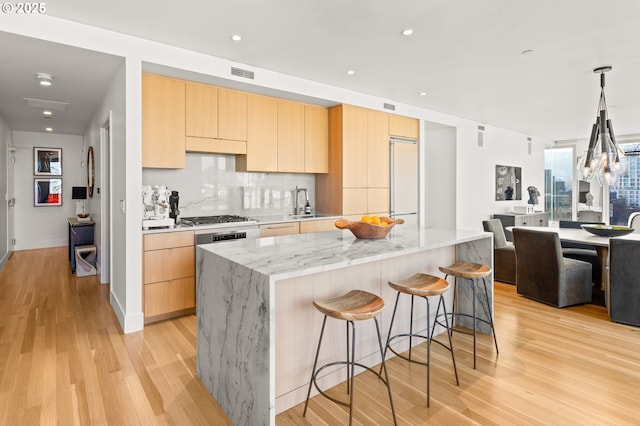 kitchen with a kitchen island, tasteful backsplash, light stone countertops, light brown cabinets, and light wood-type flooring