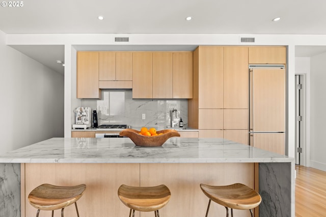 kitchen featuring sink, paneled built in refrigerator, light stone counters, tasteful backsplash, and light brown cabinets