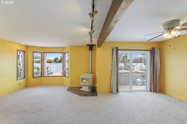 26400 NW St Helens Rd Unit 57, Scappoose, OR 97056 - unfurnished living room featuring a wood stove, a ceiling fan, a water view, carpet floors, and a textured ceiling