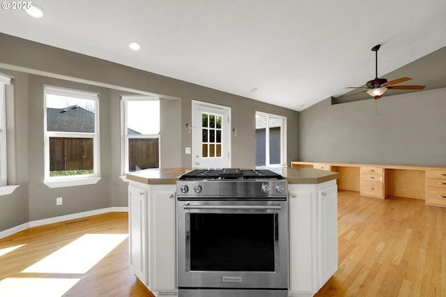 kitchen with white cabinets, stainless steel range with gas stovetop, built in desk, and light wood-style flooring