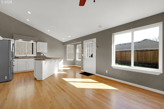 kitchen with a sink, a center island, light wood-style floors, white cabinets, and vaulted ceiling
