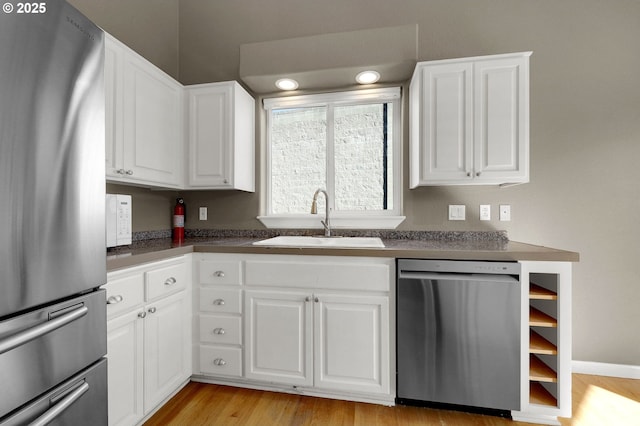 kitchen with a sink, stainless steel appliances, dark countertops, and white cabinets