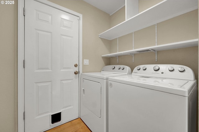 clothes washing area with laundry area, washer and dryer, and light wood-style flooring