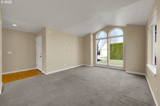 carpeted empty room featuring baseboards and vaulted ceiling