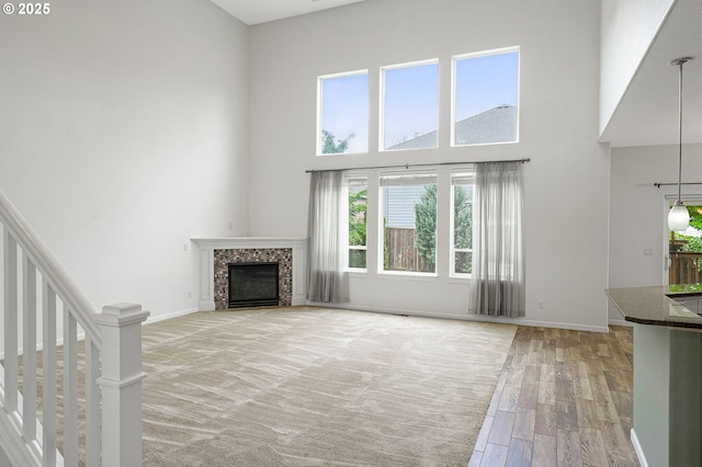 unfurnished living room featuring a towering ceiling, a tiled fireplace, light wood-style flooring, baseboards, and stairs