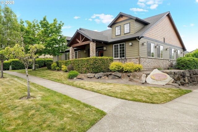 view of front of home with stone siding, a front yard, and a shingled roof