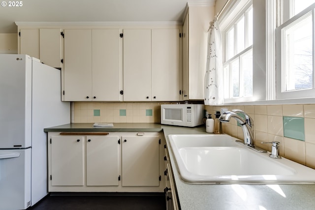 kitchen featuring white cabinets, light countertops, a sink, white appliances, and tasteful backsplash