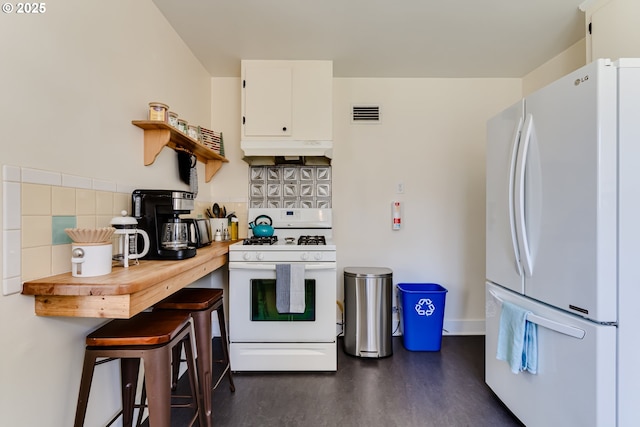 kitchen with white cabinets, under cabinet range hood, white appliances, and dark wood finished floors