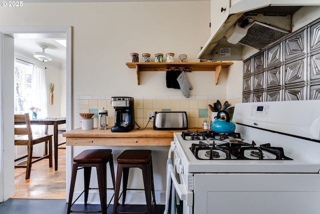 kitchen featuring white gas range oven, tile walls, open shelves, under cabinet range hood, and wooden counters