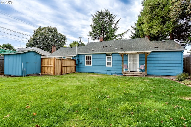 rear view of property featuring fence, an outdoor structure, a lawn, a storage unit, and roof with shingles