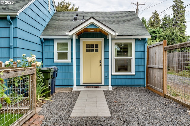 entrance to property with a shingled roof and fence