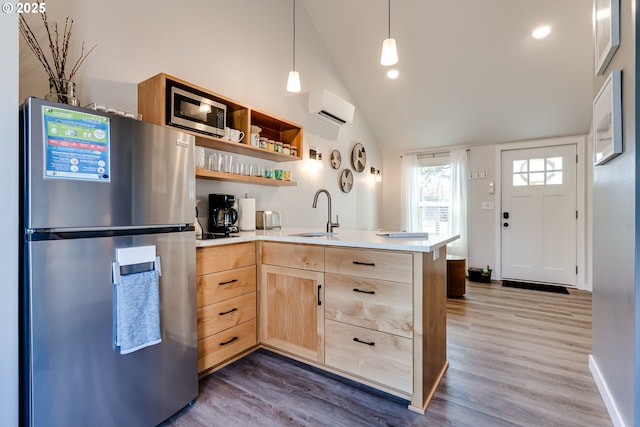 kitchen with stainless steel appliances, wood finished floors, an AC wall unit, light brown cabinets, and a sink