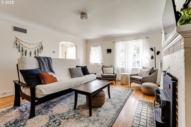 living room with arched walkways, visible vents, light wood finished floors, and a fireplace