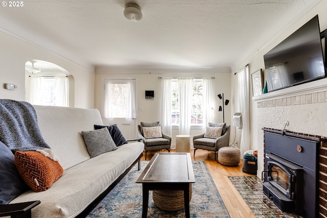 living room with ornamental molding, wood finished floors, arched walkways, and a wood stove