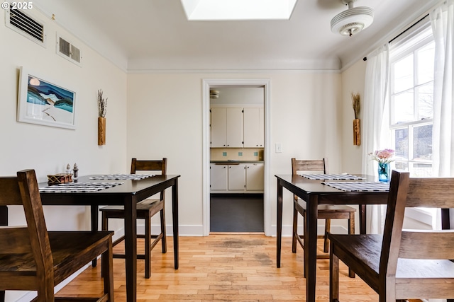 dining area with light wood-style floors, visible vents, and a skylight