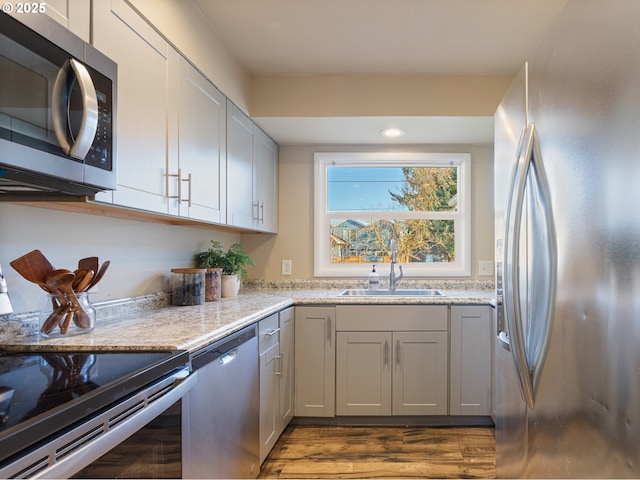 kitchen with dark wood-type flooring, appliances with stainless steel finishes, sink, and light stone counters