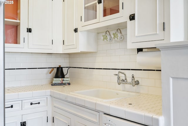 kitchen featuring glass insert cabinets, white cabinetry, a sink, and backsplash