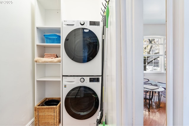 clothes washing area featuring wood finished floors, stacked washer and clothes dryer, baseboards, and laundry area