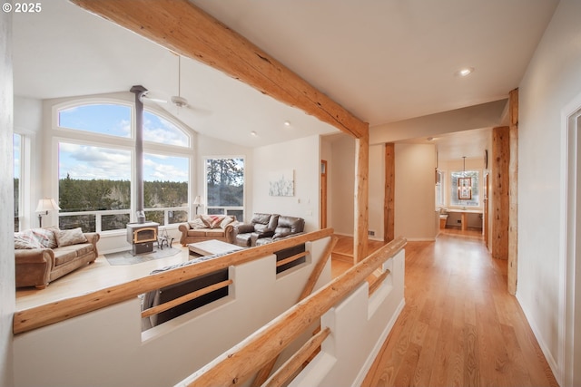 living room featuring a ceiling fan, a wood stove, vaulted ceiling with beams, light wood-style floors, and recessed lighting