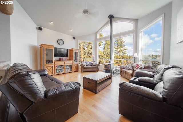 living area featuring lofted ceiling, ceiling fan, light wood-type flooring, and a wood stove