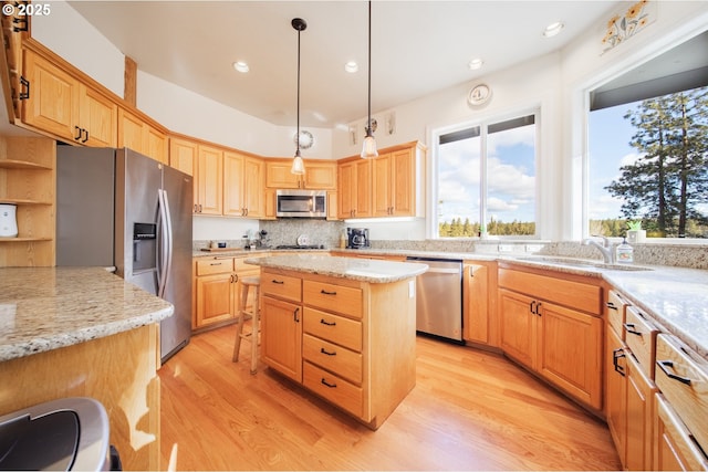 kitchen featuring light stone counters, stainless steel appliances, a sink, light wood-style floors, and a center island