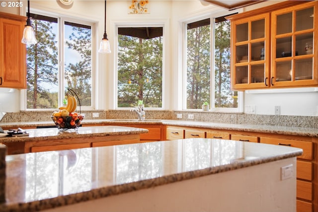 kitchen with a wealth of natural light, a sink, glass insert cabinets, and light stone countertops