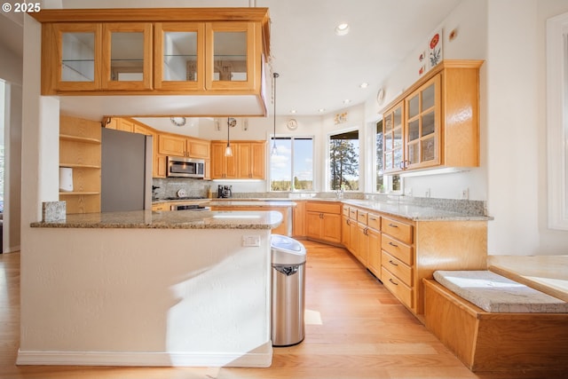 kitchen featuring tasteful backsplash, appliances with stainless steel finishes, a peninsula, light stone countertops, and light wood-type flooring