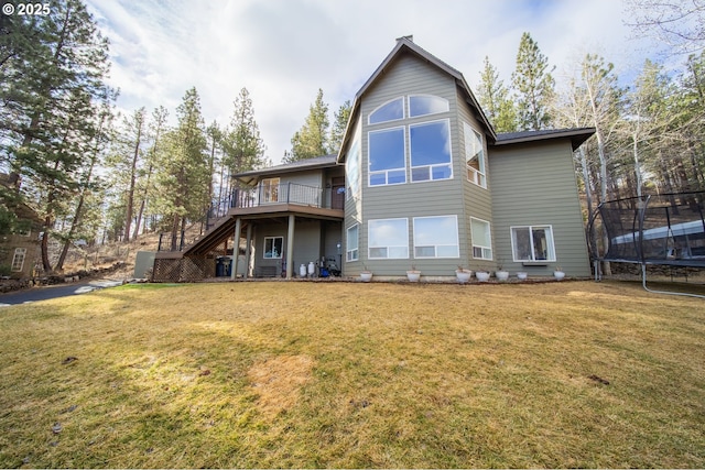 rear view of property with a trampoline, a yard, stairway, and a deck