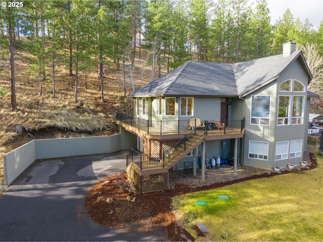 view of front of property featuring a deck, stairs, driveway, a chimney, and a front yard