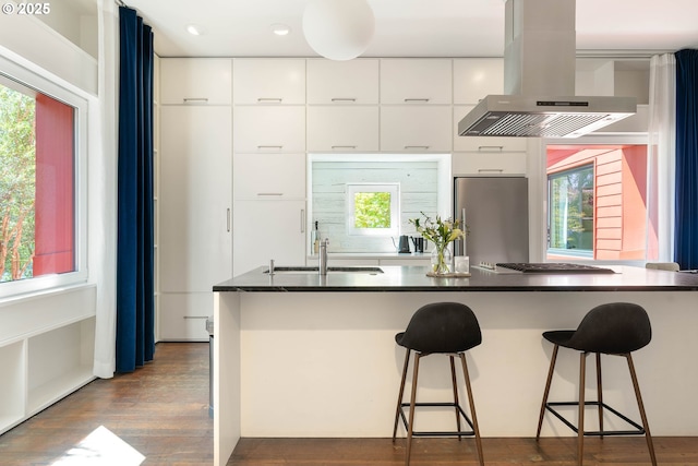 kitchen featuring island range hood, appliances with stainless steel finishes, a sink, dark countertops, and white cabinetry