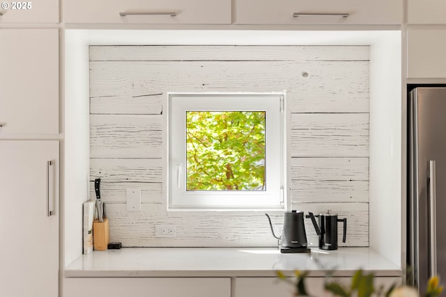 kitchen view of stainless steel refrigerator, backsplash, light countertops, and white cabinetry
