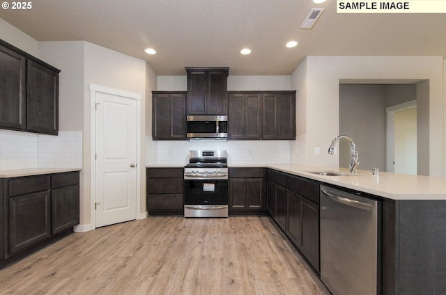 kitchen featuring stainless steel appliances, sink, light wood-type flooring, kitchen peninsula, and dark brown cabinetry