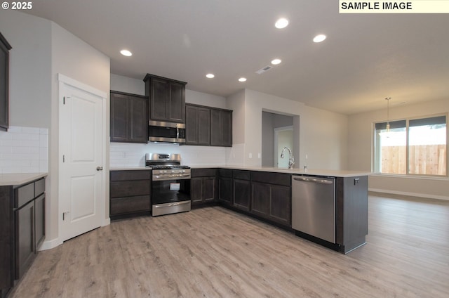 kitchen featuring kitchen peninsula, pendant lighting, light hardwood / wood-style floors, tasteful backsplash, and appliances with stainless steel finishes