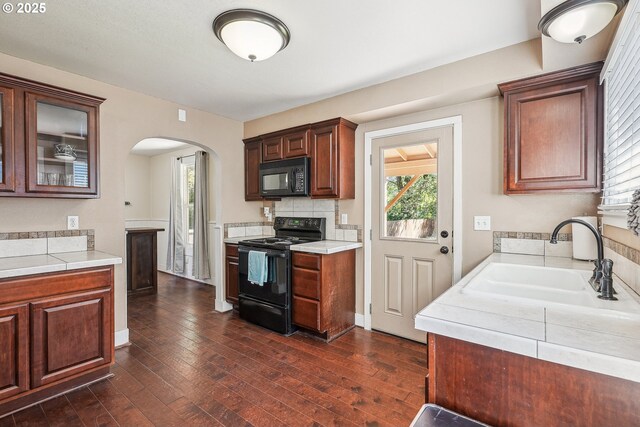 kitchen featuring a sink, light countertops, arched walkways, dark wood finished floors, and black appliances