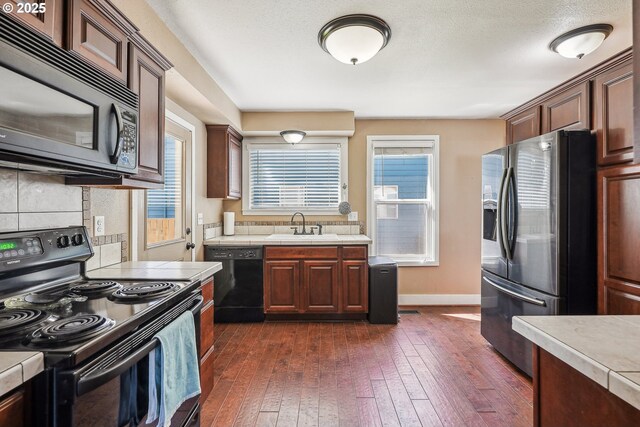 kitchen with tile counters, dark wood-style floors, black appliances, and tasteful backsplash