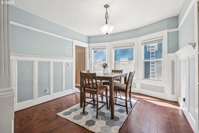 dining space with a decorative wall, dark wood-style floors, and a wealth of natural light